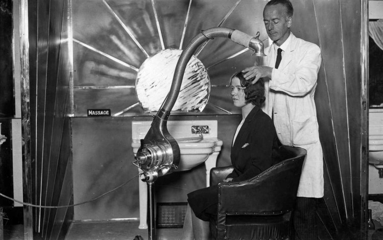 1929 г. Стилист использует автономный регулируемый фен для сушки волос клиентки в Лондоне. девушки, мода, фен