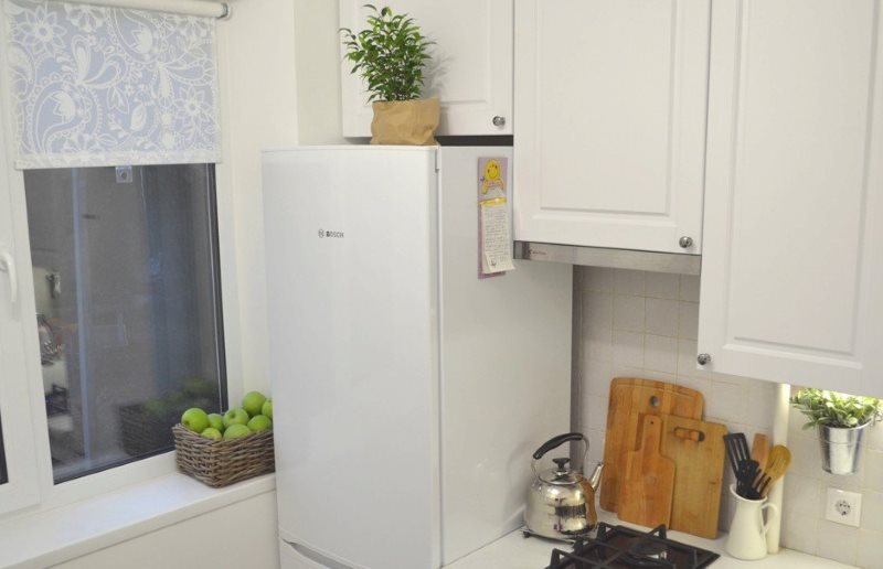 Белый холодильник возле кухонного окна