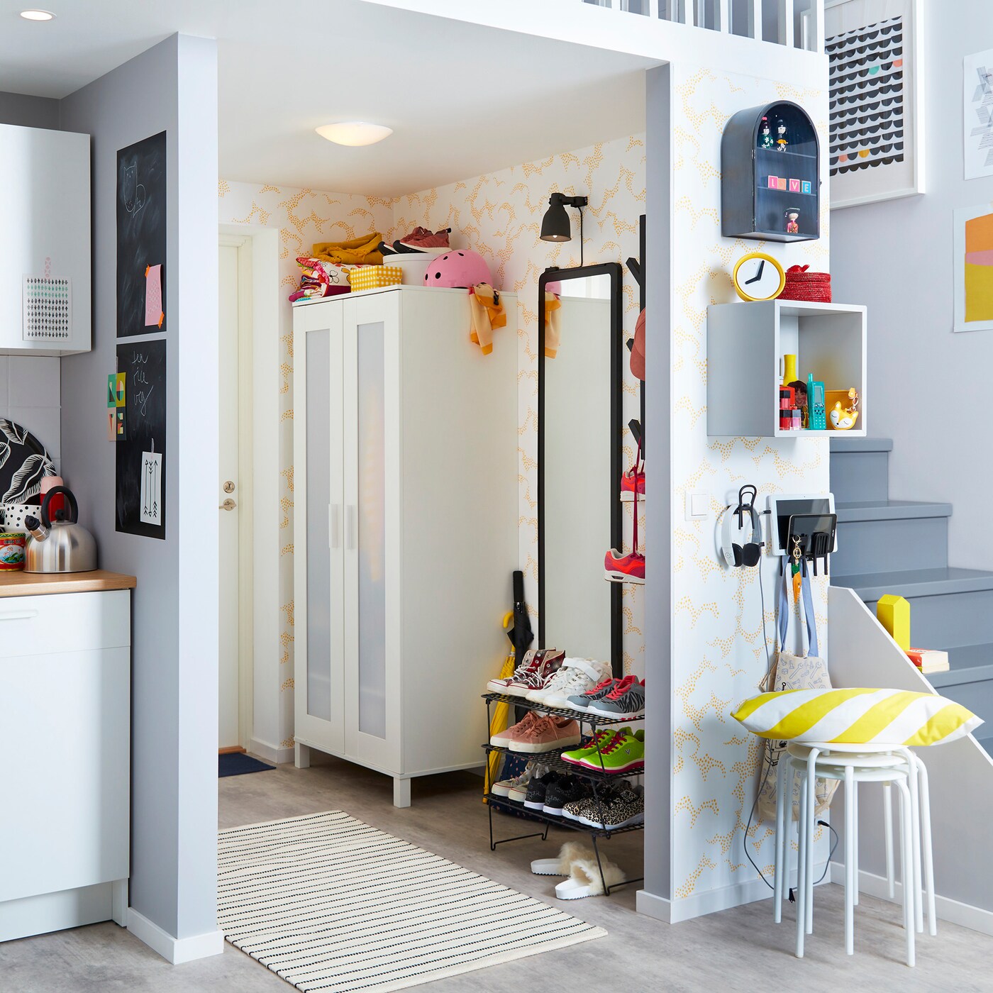 A hallway with ANEBODA wardrobe, a GREJIG shoe rack, a mirror and a white carpet on the floor and stairs in the background.